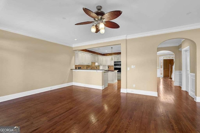 unfurnished living room featuring arched walkways, crown molding, dark wood-type flooring, and a ceiling fan