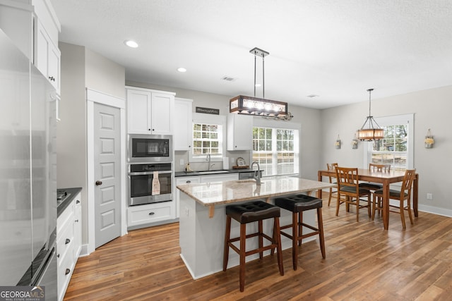 kitchen featuring an island with sink, a sink, wood finished floors, white cabinetry, and stainless steel appliances