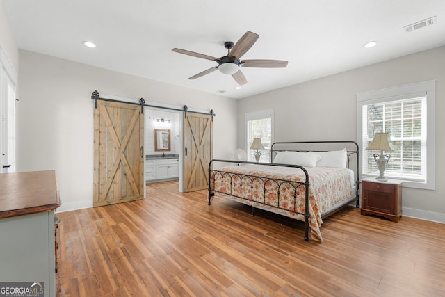 bedroom featuring visible vents, recessed lighting, a barn door, light wood-style floors, and baseboards