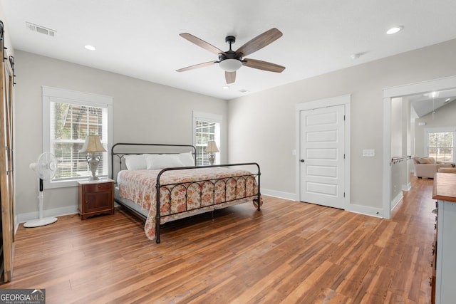 bedroom with a barn door, wood finished floors, visible vents, and baseboards