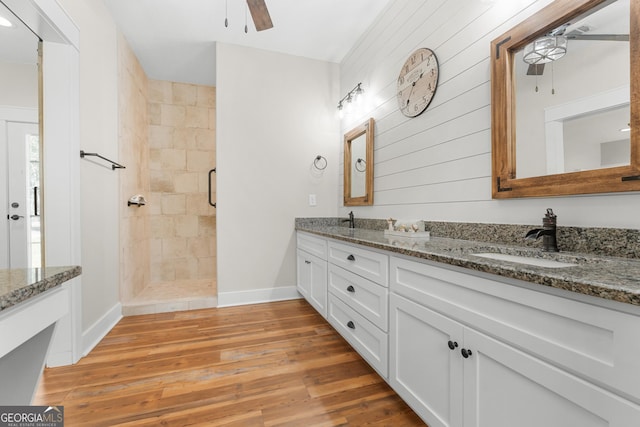 full bathroom with a stall shower, a sink, wood finished floors, double vanity, and ceiling fan