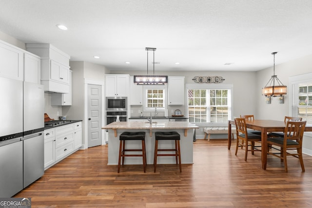 kitchen featuring a breakfast bar, appliances with stainless steel finishes, wood finished floors, hanging light fixtures, and white cabinets