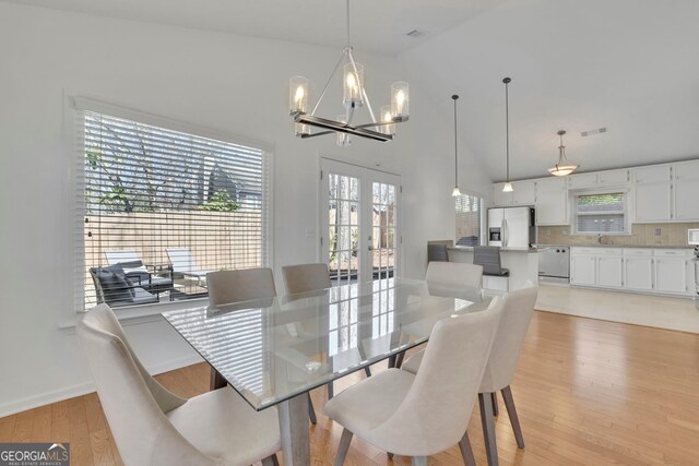 dining room with visible vents, light wood-type flooring, french doors, an inviting chandelier, and a towering ceiling