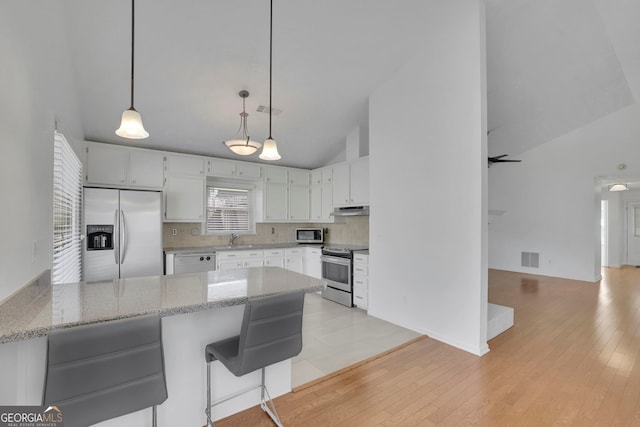 kitchen with under cabinet range hood, stainless steel appliances, light stone countertops, and a peninsula