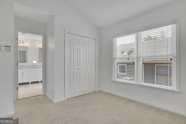 unfurnished bedroom with light carpet, ensuite bathroom, a closet, baseboards, and vaulted ceiling