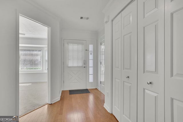 foyer entrance featuring crown molding, baseboards, visible vents, and light wood-type flooring