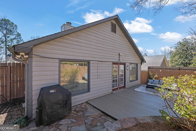 rear view of house featuring a chimney, french doors, a wooden deck, and a fenced backyard