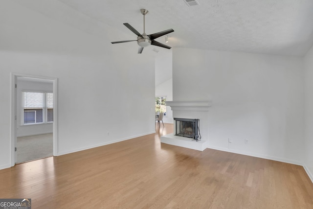 unfurnished living room featuring a ceiling fan, wood finished floors, baseboards, a fireplace with raised hearth, and a textured ceiling