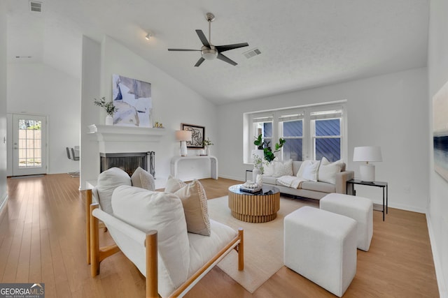 living room featuring visible vents, light wood-style flooring, a fireplace, ceiling fan, and vaulted ceiling