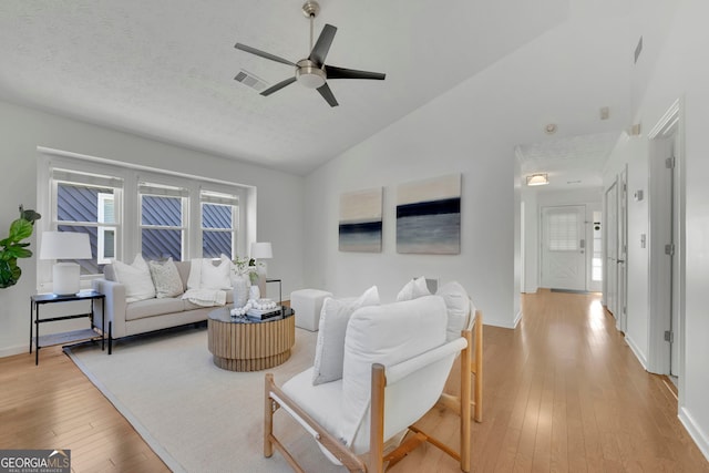 living area featuring visible vents, a textured ceiling, light wood-type flooring, and lofted ceiling