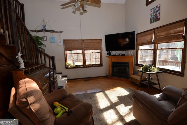 living room featuring a ceiling fan, wood finished floors, a fireplace, a towering ceiling, and stairs