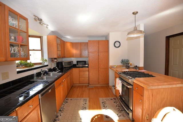 kitchen featuring light wood-style flooring, a sink, tile countertops, stainless steel appliances, and glass insert cabinets