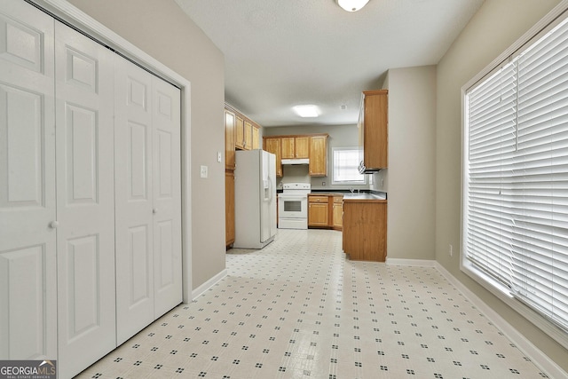 kitchen featuring under cabinet range hood, light floors, white appliances, and baseboards