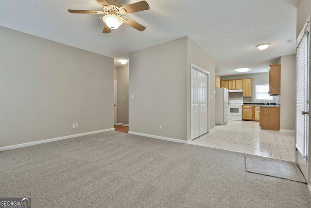 unfurnished living room with ceiling fan, light colored carpet, baseboards, and a sink