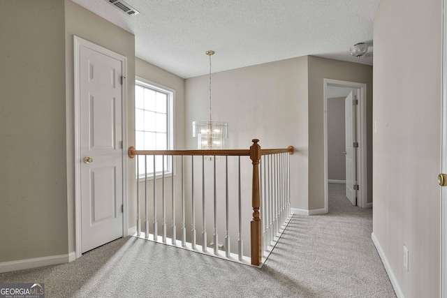 hallway featuring an inviting chandelier, visible vents, carpet floors, and a textured ceiling