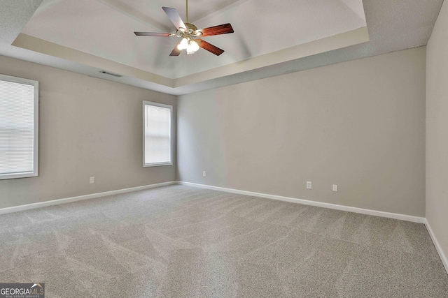 empty room with baseboards, visible vents, ceiling fan, a raised ceiling, and carpet flooring