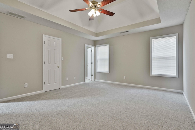 carpeted empty room with visible vents, baseboards, and a tray ceiling