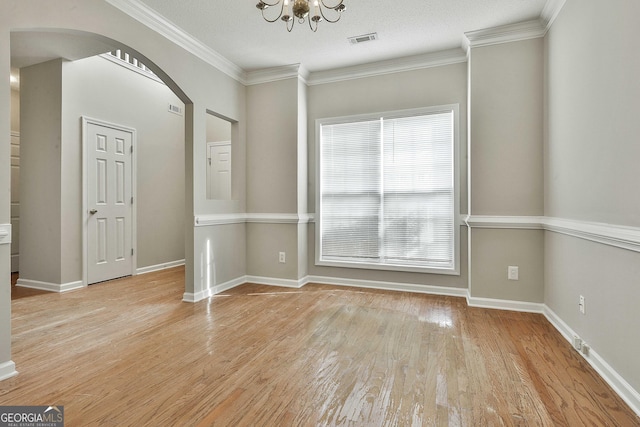 empty room featuring light wood-type flooring, visible vents, arched walkways, and crown molding