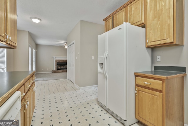 kitchen featuring dark countertops, a fireplace with raised hearth, baseboards, open floor plan, and white appliances