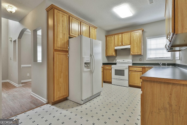 kitchen featuring under cabinet range hood, a sink, white appliances, arched walkways, and light floors