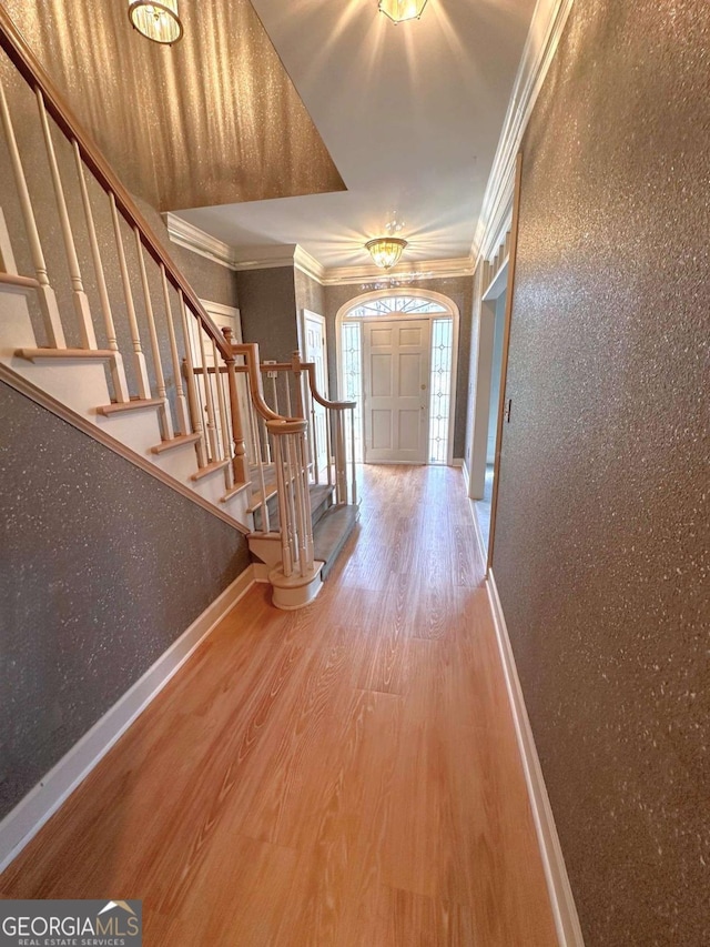 foyer featuring baseboards, wood finished floors, ornamental molding, and stairway