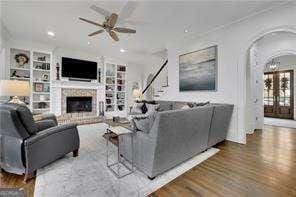 living room featuring built in shelves, ceiling fan, a fireplace, wood finished floors, and arched walkways