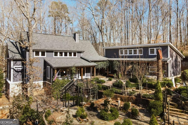 back of property featuring stairway, a chimney, and roof with shingles