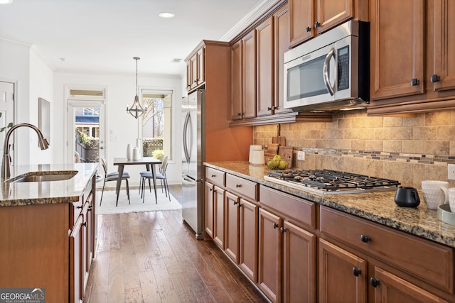 kitchen featuring a sink, light stone counters, stainless steel appliances, brown cabinetry, and decorative backsplash