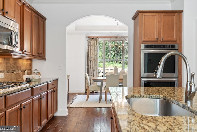 kitchen featuring brown cabinets, ornamental molding, a sink, backsplash, and appliances with stainless steel finishes