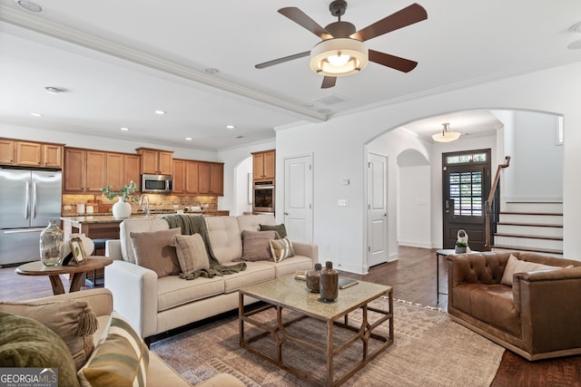 living room featuring visible vents, a ceiling fan, arched walkways, crown molding, and dark wood-style flooring