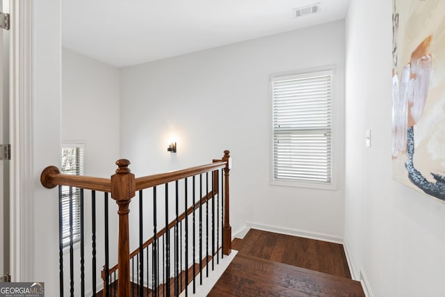 hallway featuring visible vents, baseboards, dark wood finished floors, an upstairs landing, and a wealth of natural light