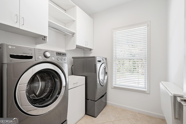 clothes washing area with washer and clothes dryer, cabinet space, baseboards, and light tile patterned flooring