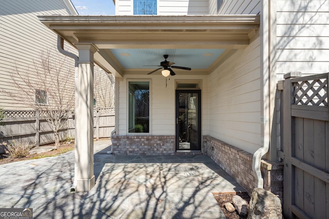 view of exterior entry featuring a patio area, brick siding, a ceiling fan, and fence