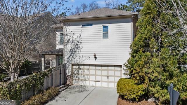 view of property exterior featuring driveway, a shingled roof, a garage, and fence