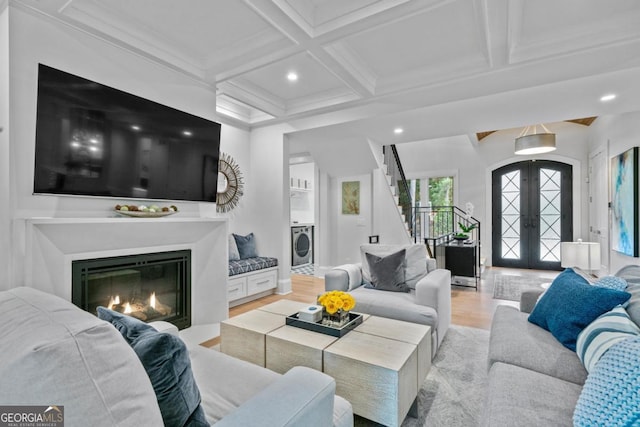 living area featuring light wood-type flooring, stairs, french doors, a glass covered fireplace, and washer / clothes dryer