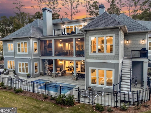 back of house at dusk featuring a balcony, fence private yard, a patio area, and a chimney