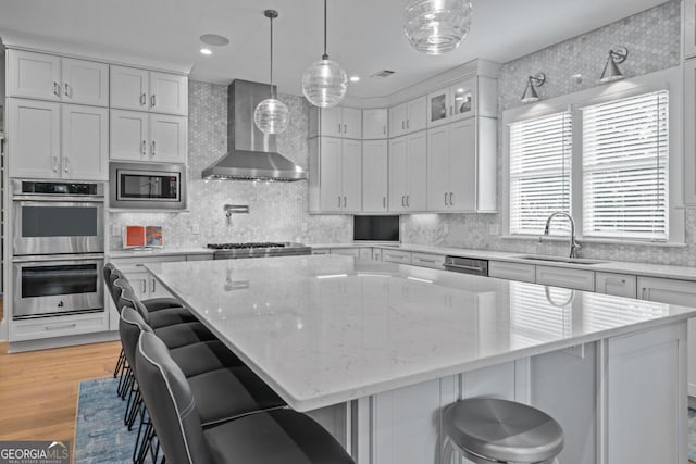 kitchen with a sink, appliances with stainless steel finishes, wall chimney exhaust hood, and white cabinetry