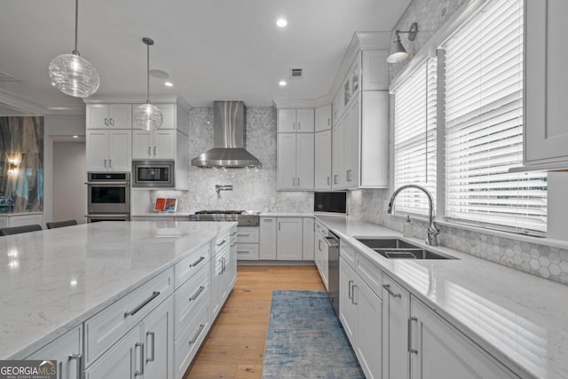 kitchen featuring white cabinets, wall chimney exhaust hood, appliances with stainless steel finishes, and a sink