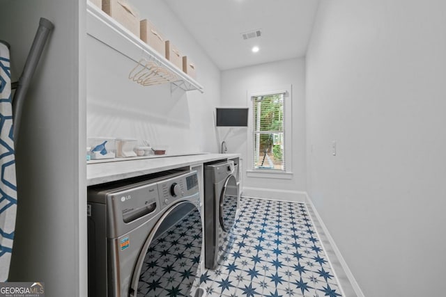 washroom with visible vents, baseboards, light floors, laundry area, and washing machine and clothes dryer