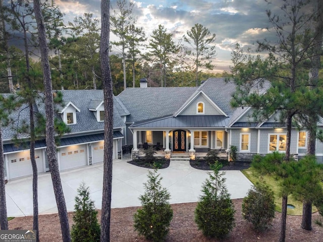 view of front of house with driveway, french doors, roof with shingles, covered porch, and a garage