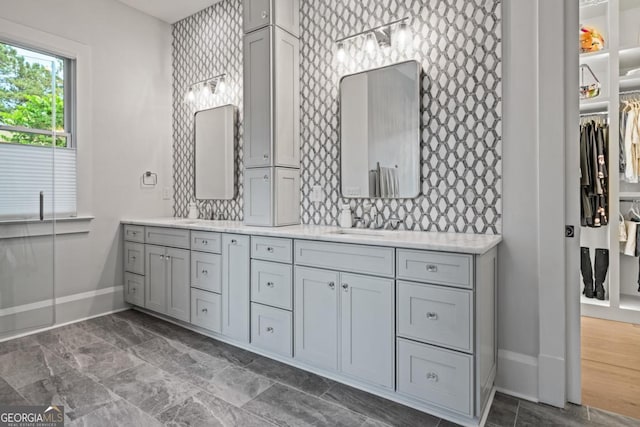 full bathroom featuring baseboards, double vanity, a sink, a walk in closet, and tasteful backsplash