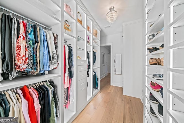 spacious closet with visible vents, an inviting chandelier, and light wood finished floors