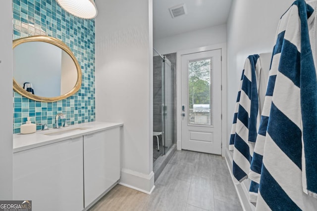 bathroom featuring vanity, baseboards, visible vents, a stall shower, and decorative backsplash