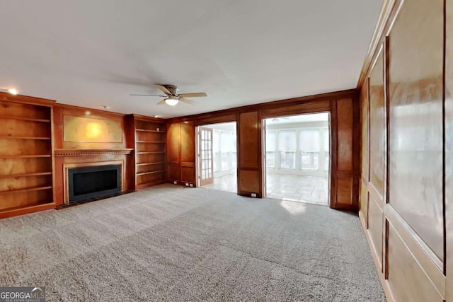 unfurnished living room featuring built in features, a fireplace with flush hearth, a decorative wall, and light carpet