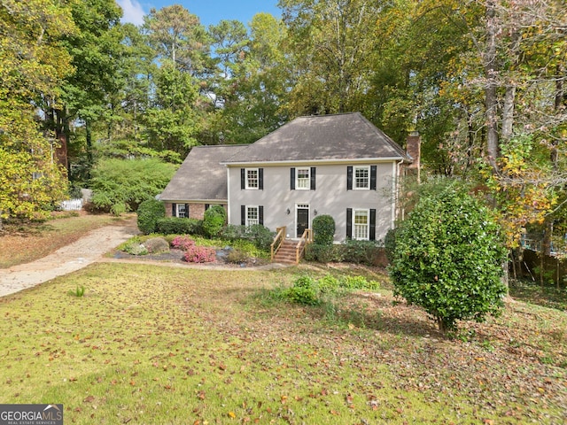 colonial home with stucco siding, driveway, a front lawn, and a chimney