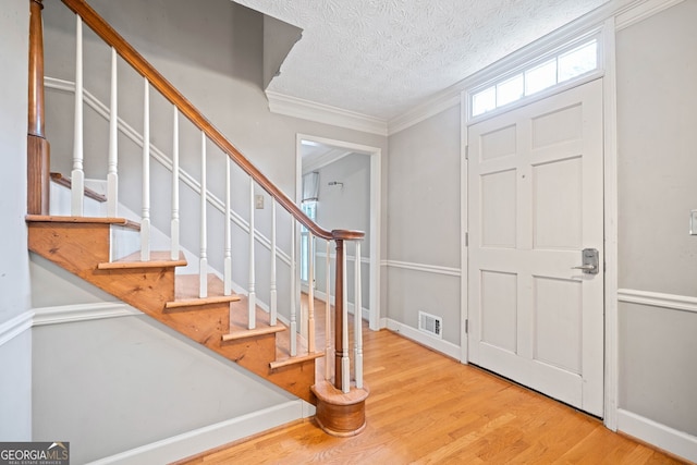 foyer entrance featuring visible vents, a textured ceiling, wood finished floors, stairway, and crown molding