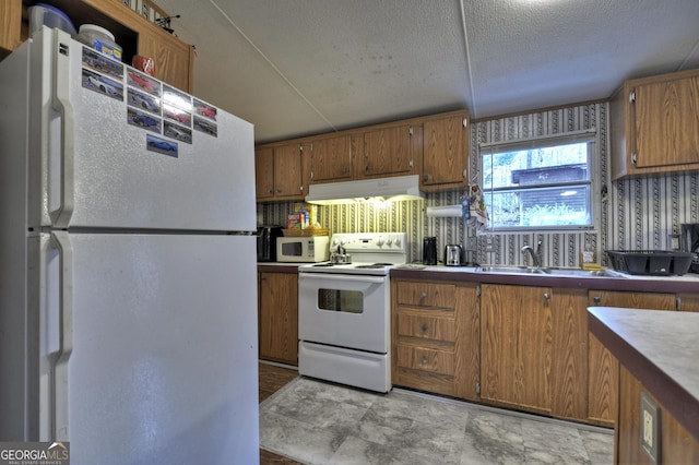 kitchen with white appliances, a sink, under cabinet range hood, a textured ceiling, and brown cabinets