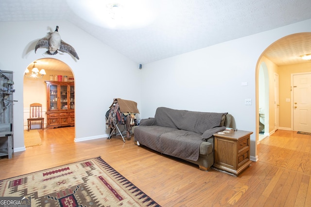 living area featuring baseboards, light wood-type flooring, lofted ceiling, arched walkways, and a notable chandelier