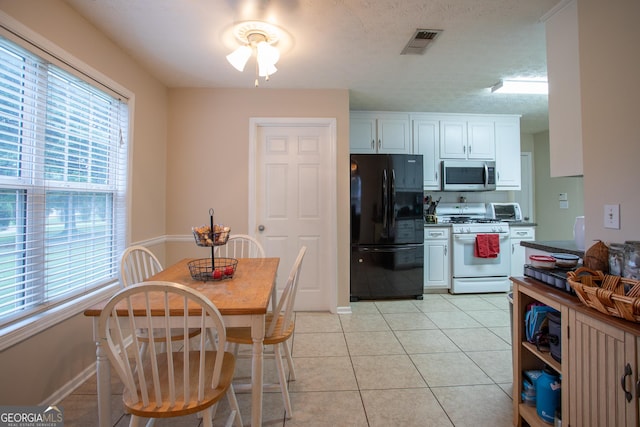 kitchen with stainless steel microwave, visible vents, gas range gas stove, light tile patterned floors, and freestanding refrigerator