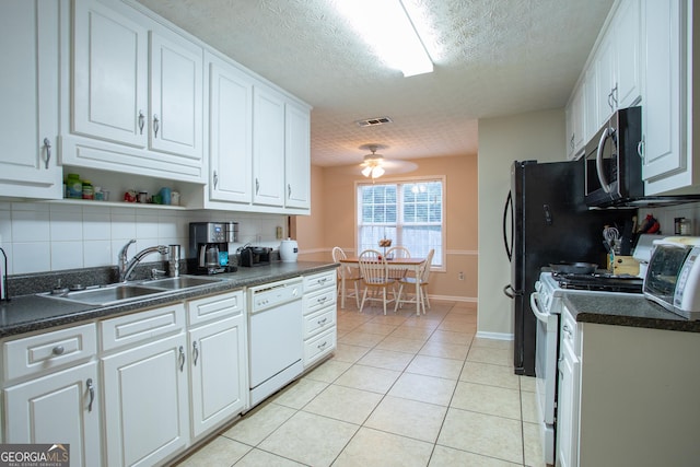 kitchen with white appliances, light tile patterned flooring, a sink, white cabinets, and dark countertops